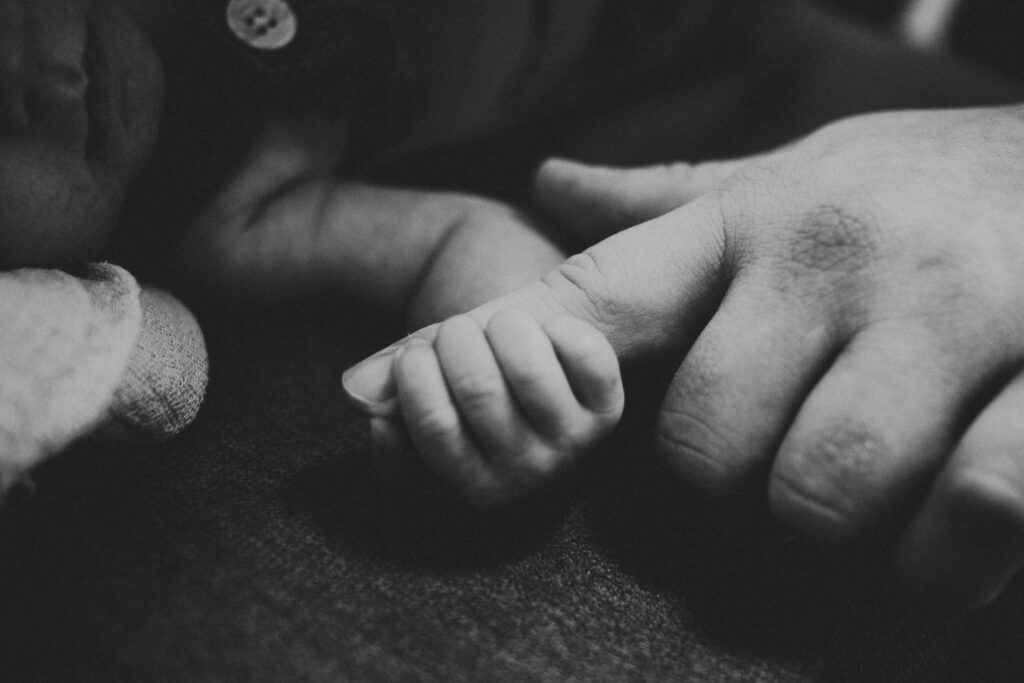 Kleine Babyhand umgreift den Finger des Vaters, intimes Schwarzweiß-Detail
