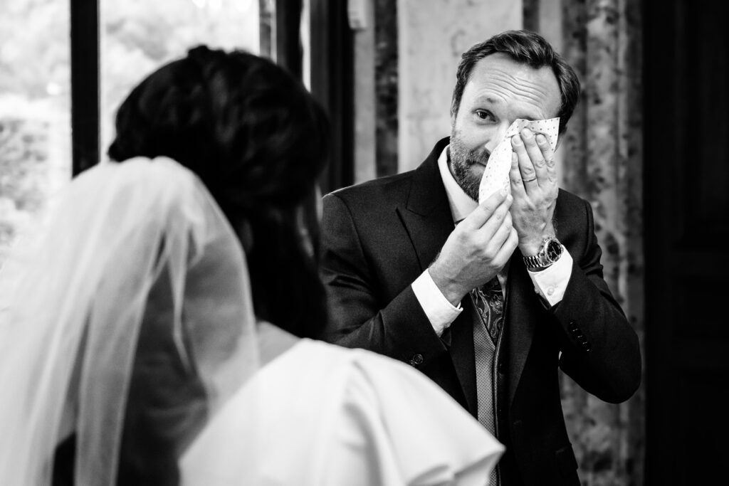 Gerührter Bräutigam wischt sich Tränen ab beim Anblick der Braut, emotionaler Moment in Schwarzweiß