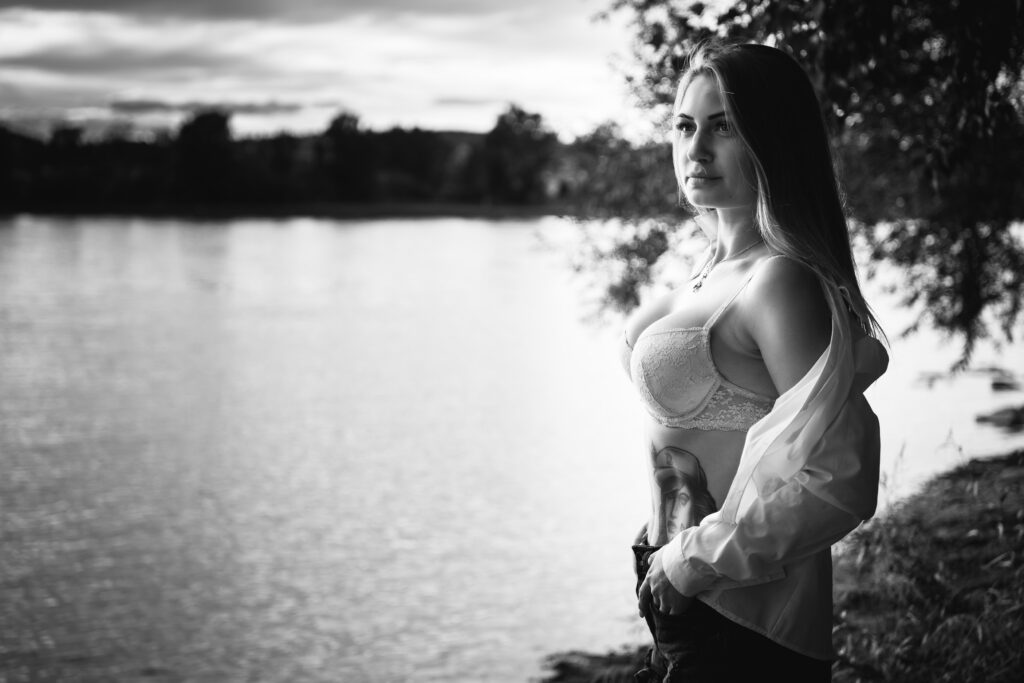 Frau mit offener Bluse am Seeufer blickt in die Ferne, stimmungsvolles Schwarzweiß-Portrait